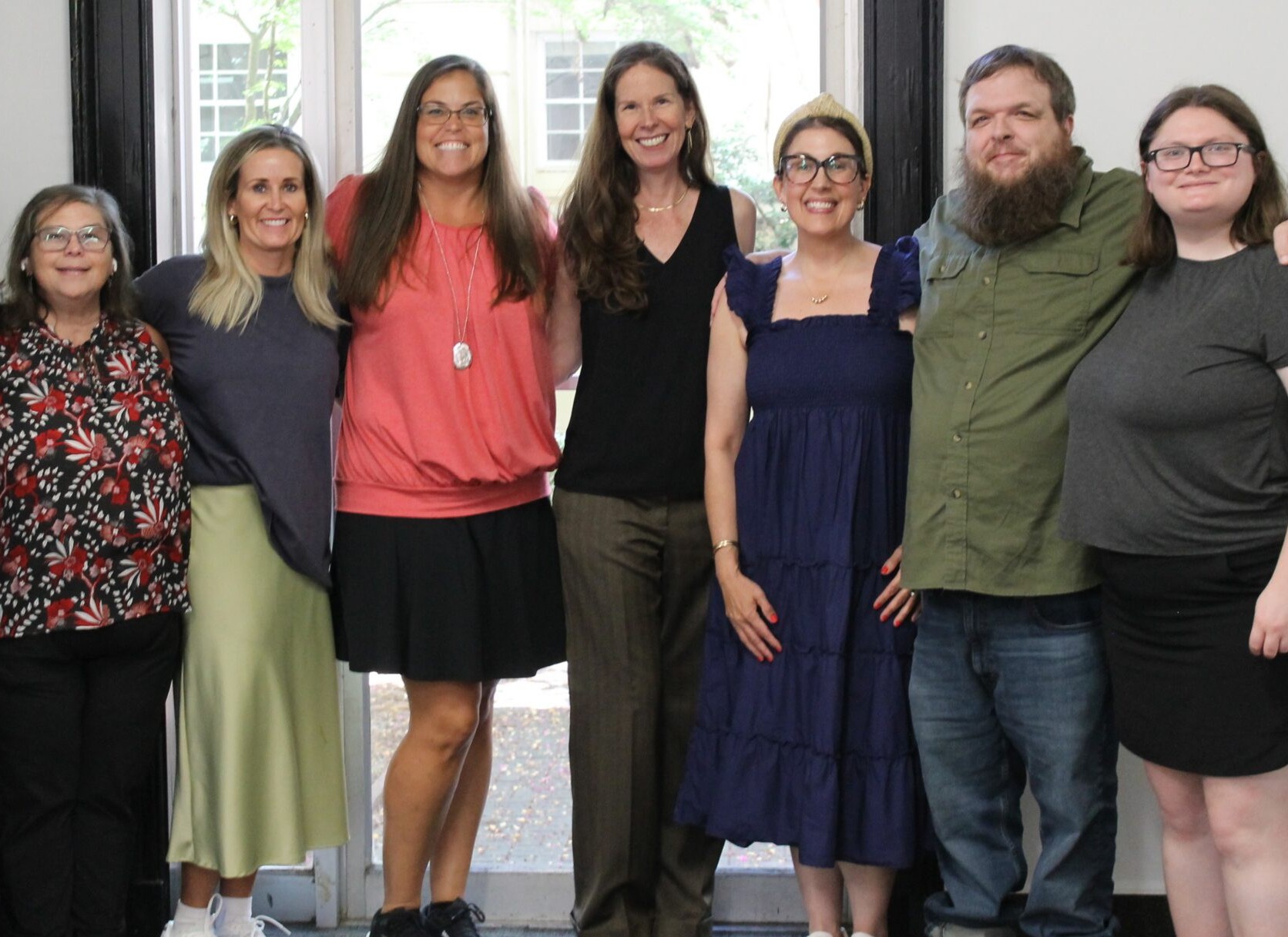 Staff Seven people standing in a row posing for a group photo indoors.
